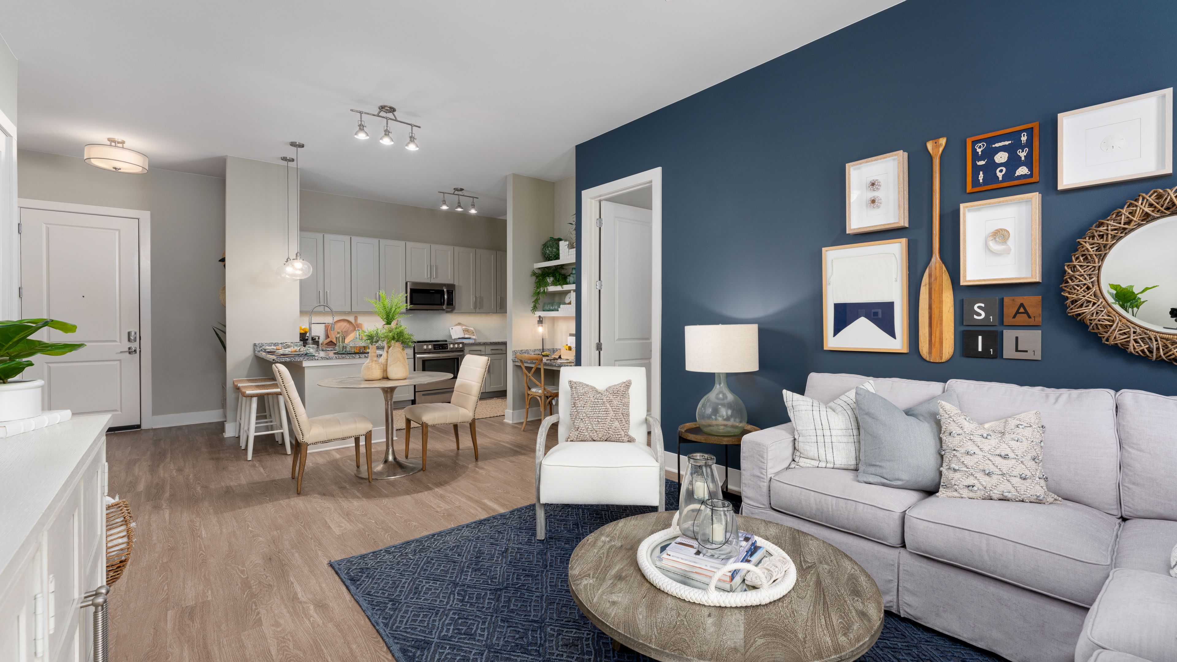 Hawthorne at Indy West apartment living space and kitchen with blue accent wall, a dining table with two chairs, a sectional couch, coffee table, and chair